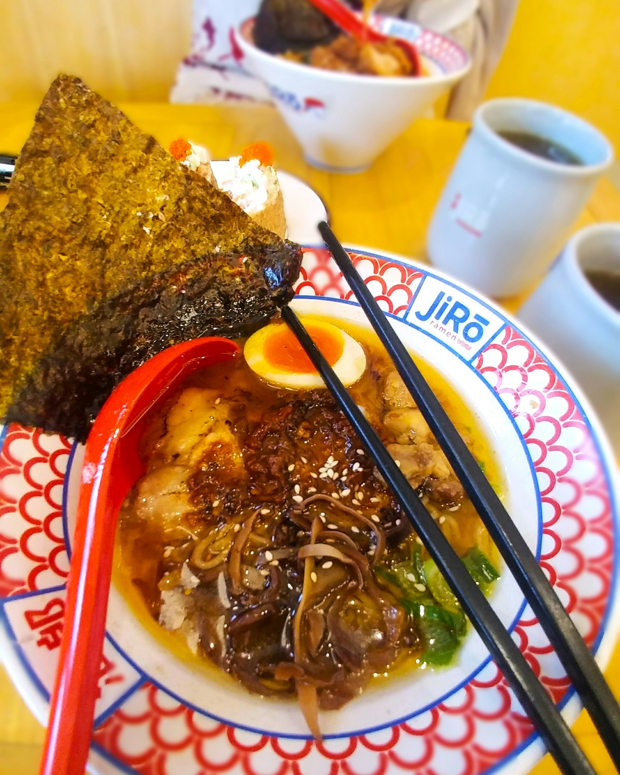 Bowl of Japanese ramen with seaweed, egg, and chopsticks on a colorful plate