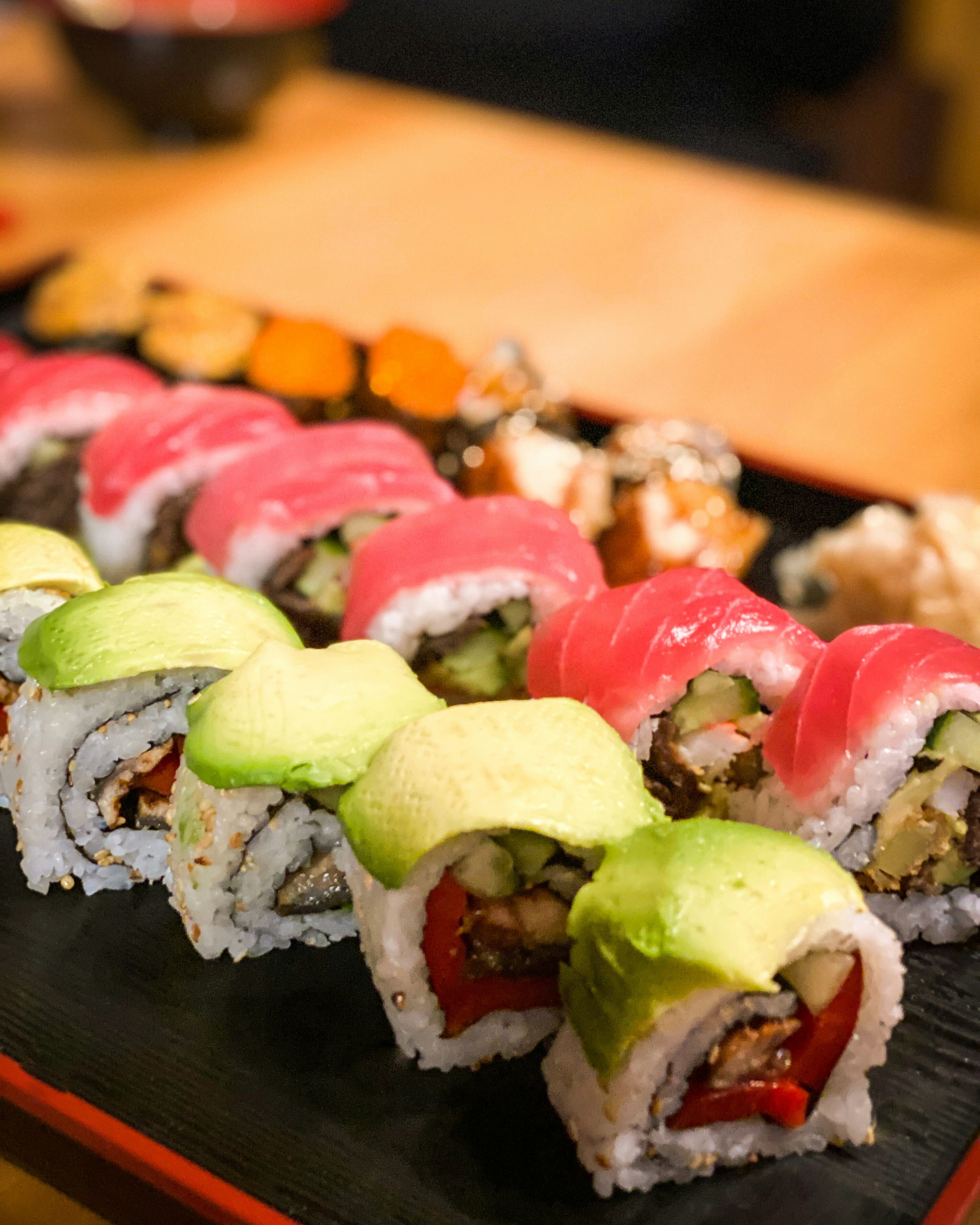 Assorted sushi rolls with avocado and tuna on a black tray